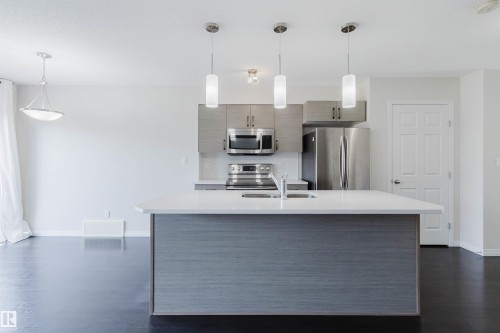 Kitchen island with white countertop, integrated sink, and three pendant lights - 2082 Price Landing, Edmonton, AB - Indoor Photo Showing Kitchen With Stainless Steel Kitchen With Upgraded Kitchen