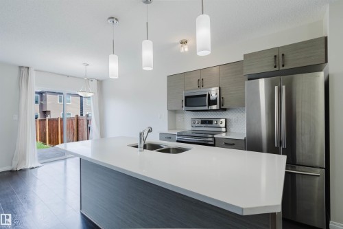 Contemporary kitchen featuring a large island with an undermount double sink, stainless steel appliances, light wood-finish cabinetry, a white subway tile backsplash, and dark wood-finish flooring - 2082 Price Landing, Edmonton, AB - Indoor Photo Showing Kitchen With Stainless Steel Kitchen With Double Sink With Upgraded Kitchen