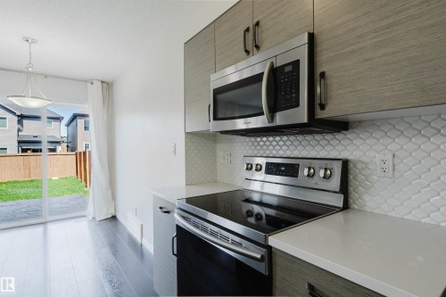 Modern kitchen featuring stainless steel appliances, light wood-finish cabinetry, a patterned tile backsplash, and light countertops - 2082 Price Landing, Edmonton, AB - Indoor Photo Showing Kitchen With Upgraded Kitchen