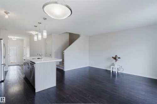 Open-concept living space featuring dark wood-finish flooring, a kitchen island with a built-in sink, stainless steel appliances, modern pendant lighting, and a staircase with carpeted treads - 2082 Price Landing, Edmonton, AB - Indoor Photo Showing Kitchen