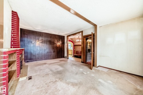 Living area featuring a red brick fireplace with built-in shelving, dark wood paneling, sconce lighting, and carpeted flooring - 11929 91 Street, Edmonton, AB 