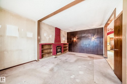 Living area featuring a red brick fireplace with an integrated shelving unit, wood panel accent wall, and wall-mounted light fixtures - 11929 91 Street, Edmonton, AB 