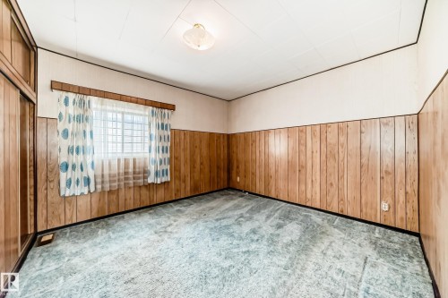 Interior room featuring wood-finish wall paneling, a single window, and a ceiling-mounted light fixture - 11929 91 Street, Edmonton, AB 
