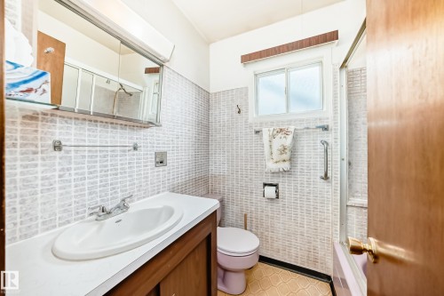 Bathroom with light-toned tiled walls, a white vanity with an integrated sink, and an overhead medicine cabinet with mirrored doors - 11929 91 Street, Edmonton, AB 