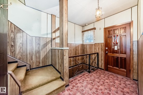 Entryway featuring wood paneling, tiled flooring, a carved wooden door, and a staircase with carpeted treads - 11929 91 Street, Edmonton, AB 