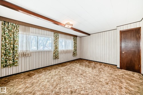 Spacious room featuring textured carpeting, vertical striped wallpaper, and multiple windows - 11929 91 Street, Edmonton, AB 