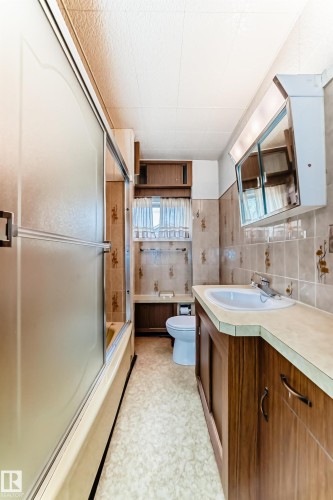 Full bathroom featuring a shower-tub combination with frosted sliding doors, a vanity with wood-finish cabinetry, a white basin, and a mirrored medicine cabinet - 11929 91 Street, Edmonton, AB 