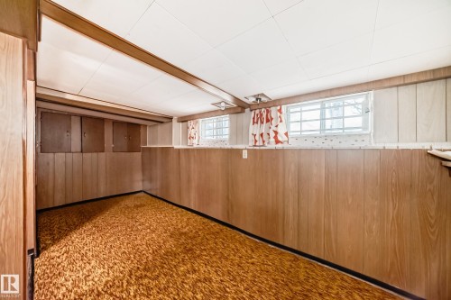 Finished room featuring wood-panel walls, patterned carpet, and multiple windows - 11929 91 Street, Edmonton, AB 