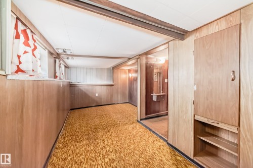 Lower-level recreation space featuring wood-paneled walls and a built-in storage cabinet with open shelving - 11929 91 Street, Edmonton, AB 