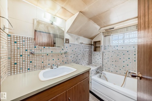 Bathroom featuring a white bathtub, glass block window, built-in shelving, and a vanity with a white basin sink and wood-finish cabinetry - 11929 91 Street, Edmonton, AB 