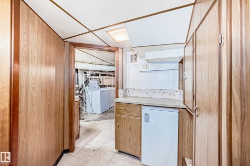 Kitchenette area featuring wood-finish cabinetry, a light-toned countertop, and a tiled backsplash - 11929 91 Street, Edmonton, AB 