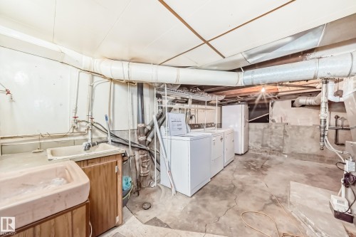 Basement utility area featuring a wall-mounted sink, exposed piping, and a concrete floor - 11929 91 Street, Edmonton, AB 