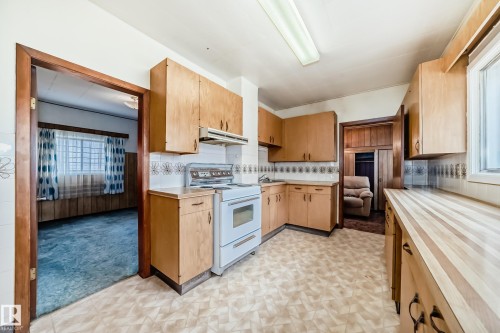 Kitchen featuring wood-finish cabinetry, patterned linoleum flooring, white tile backsplash, and a white range with overhead hood - 11929 91 Street, Edmonton, AB 