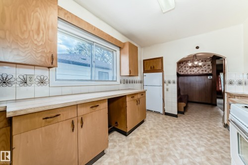 Kitchen with wood-finish cabinetry, patterned floor tiling, and a window with exterior views - 11929 91 Street, Edmonton, AB 