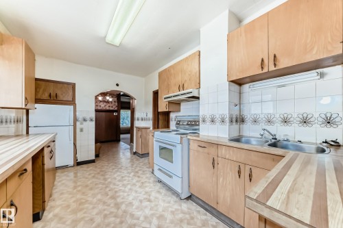 Kitchen featuring wood-finish cabinetry, patterned flooring, and a double basin stainless steel sink - 11929 91 Street, Edmonton, AB 