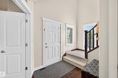 Entryway featuring a white paneled door, wood-finish flooring, a carpeted staircase with dark wood railings, and two windows with blinds - 8003 Summerside Grande Boulevard, Edmonton, AB - Indoor Photo Showing Other Room