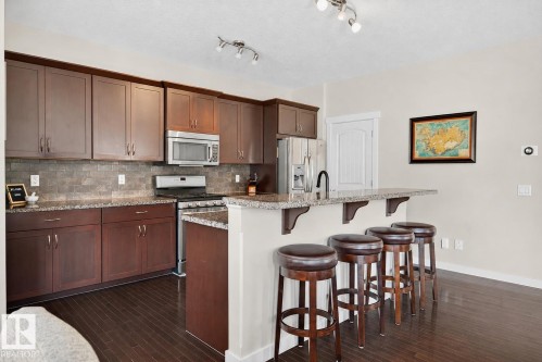 Kitchen featuring dark wood cabinetry, stainless steel appliances, granite countertops, and a tile backsplash - 8003 Summerside Grande Boulevard, Edmonton, AB - Indoor Photo Showing Kitchen