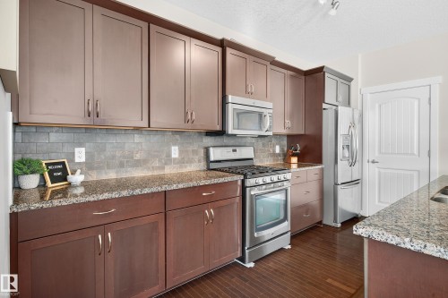 Kitchen featuring wood-finish flooring, dark wood cabinetry, and stainless steel appliances - 8003 Summerside Grande Boulevard, Edmonton, AB - Indoor Photo Showing Kitchen
