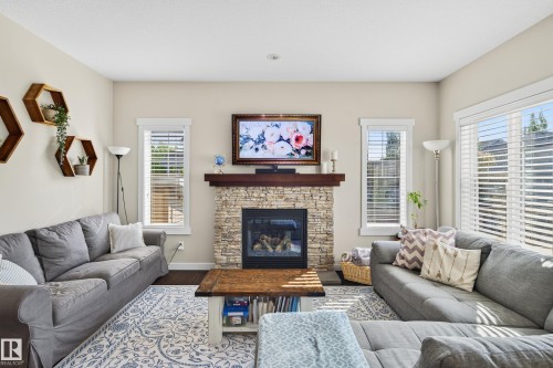 Inviting living area featuring a stacked stone fireplace with a dark wood mantle, recessed lighting, and multiple windows with blinds - 8003 Summerside Grande Boulevard, Edmonton, AB - Indoor Photo Showing Living Room With Fireplace
