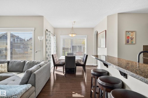 Open concept living area featuring dark wood-finish flooring, a dining area with a contemporary chandelier, a breakfast bar with stone countertop, and multiple windows with blinds - 8003 Summerside Grande Boulevard, Edmonton, AB - Indoor Photo Showing Other Room