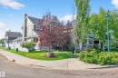 Corner property featuring a light-toned exterior with stone accents, an inviting front porch with white railings, and mature trees providing natural shading - 8003 Summerside Grande Boulevard, Edmonton, AB  - Outdoor 