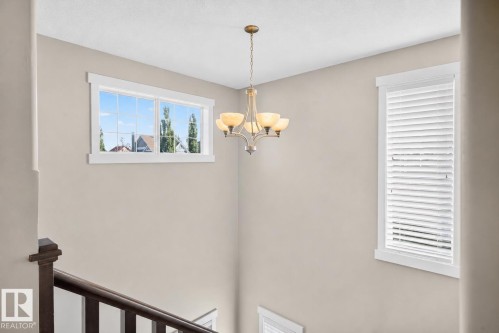 Stairwell featuring a bronze chandelier, white trim windows, and wood banister - 8003 Summerside Grande Boulevard, Edmonton, AB - Indoor Photo Showing Other Room