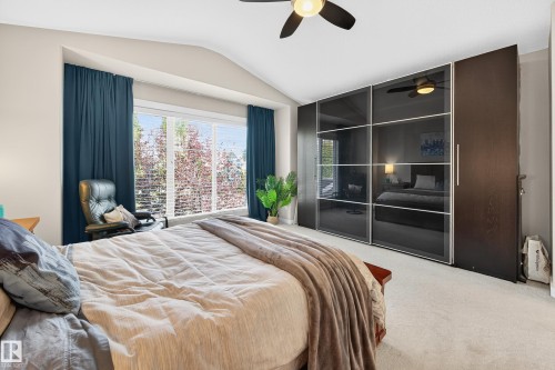Spacious room with a vaulted ceiling, large picture window with horizontal blinds, built-in wardrobe with dark wood-finish and frosted glass panels, and a ceiling fan - 8003 Summerside Grande Boulevard, Edmonton, AB - Indoor Photo Showing Bedroom