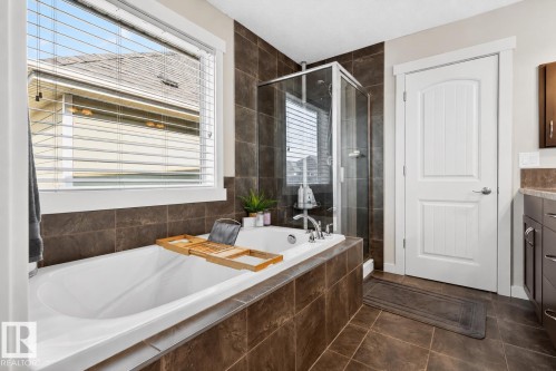 Built-in bathtub with chrome fixtures, surrounded by large format brown tile - 8003 Summerside Grande Boulevard, Edmonton, AB - Indoor Photo Showing Bathroom