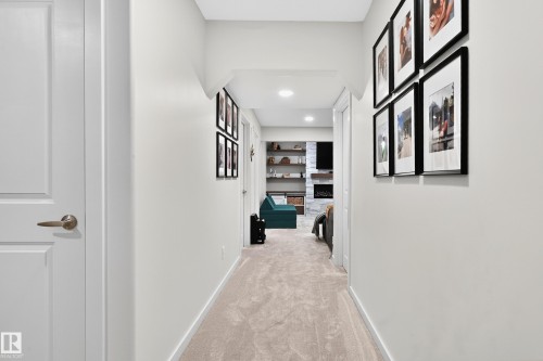 Hallway with light-toned carpet flooring and white painted walls leading to a room with a stone-clad fireplace, integrated shelving, and recessed lighting - 8003 Summerside Grande Boulevard, Edmonton, AB - Indoor Photo Showing Other Room