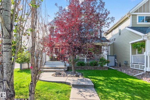 Traditional-style home featuring a covered front porch with white railing, stone facade accents, mature landscaping, and a concrete pathway - 8003 Summerside Grande Boulevard, Edmonton, AB - Outdoor