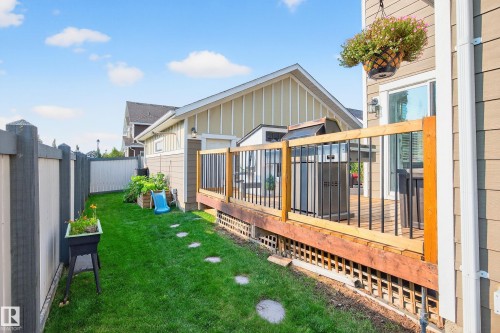 Exterior deck with wood railing and black metal balusters, featuring a sliding glass door and an attached wall sconce - 8003 Summerside Grande Boulevard, Edmonton, AB - Outdoor
