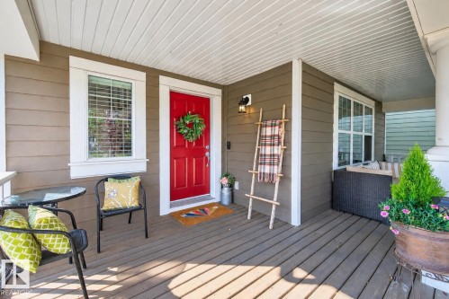 Covered front porch with wood-finish decking, tan siding, and a vibrant red entry door - 8003 Summerside Grande Boulevard, Edmonton, AB - Outdoor With Deck Patio Veranda With Exterior