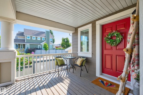 Covered porch featuring a red entry door with white trim, wood-finish flooring, and a white balustrade - 8003 Summerside Grande Boulevard, Edmonton, AB - Outdoor With Deck Patio Veranda With Exterior