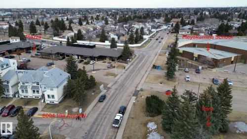 Aerial view showcasing the property's location within a developed neighborhood, featuring commercial buildings, residential structures, and established trees - 6004 19A Avenue Nw, Edmonton, AB 