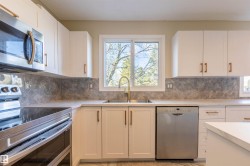 Kitchen featuring white cabinetry with bronze hardware, a stainless steel microwave, a stainless steel dishwasher, a gold-finish sink faucet, and a large window above the sink - 