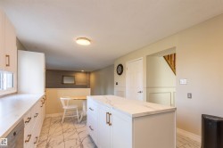 Kitchen featuring white cabinetry with gold-finish hardware, a matching center island, and stone-look tile flooring - 