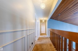 Hallway featuring wainscoting, wood-finish railing, and two orb pendant lights - 
