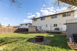Expansive grassy backyard featuring a built-in fire pit, privacy fencing, and a multi-level wood deck with white railings - 