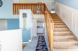 Carpeted staircase with wood railing, leading to a second-story landing with a matching wood banister - 