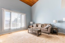 Living room featuring a vaulted wood-paneled ceiling, large picture windows with vertical blinds, and light blue wall finishes - 