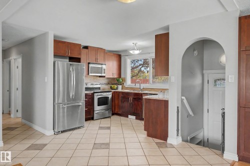 Dining area with kitchen featuring wood-finish cabinetry, stainless steel appliances, and a tiled backsplash - 16715 79A Avenue, Edmonton, AB - Indoor Photo Showing Kitchen With Stainless Steel Kitchen