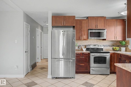 Kitchen featuring stainless steel appliances, wood cabinetry, granite-look countertops, and a stone-tile backsplash - 16715 79A Avenue, Edmonton, AB - Indoor Photo Showing Kitchen With Stainless Steel Kitchen
