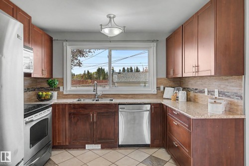 Kitchen featuring rich wood cabinetry, stone countertops, a tiled backsplash, and stainless steel appliances - 16715 79A Avenue, Edmonton, AB - Indoor Photo Showing Kitchen With Double Sink