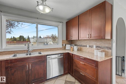 Kitchen featuring wood cabinetry, stone countertops, a stainless steel dishwasher, and a double basin sink with a gooseneck faucet - 16715 79A Avenue, Edmonton, AB - Indoor Photo Showing Kitchen With Double Sink