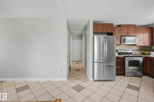 Kitchen featuring stainless steel appliances, wood cabinetry, tile flooring with accent squares, and a tiled backsplash - 16715 79A Avenue, Edmonton, AB - Indoor Photo Showing Kitchen With Stainless Steel Kitchen