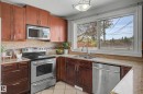 Kitchen featuring wood cabinetry, stainless steel appliances, a double basin sink with a gooseneck faucet, light-toned countertops, and a decorative tile backsplash - 16715 79A Avenue, Edmonton, AB  - Indoor Photo Showing Kitchen With Double Sink 