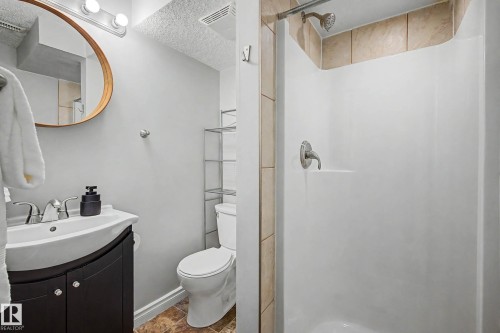 Full bathroom featuring a shower with tile surround, a dark wood-finish vanity with a white ceramic sink, a round wood-frame mirror, and neutral wall paint - 16715 79A Avenue, Edmonton, AB - Indoor Photo Showing Bathroom