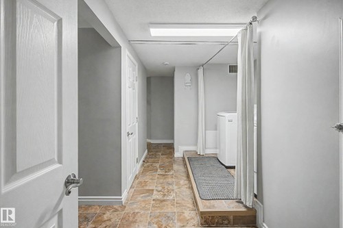 Utility area featuring a raised platform with appliances, privacy curtain, and tile flooring - 16715 79A Avenue, Edmonton, AB - Indoor Photo Showing Other Room