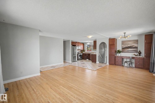 Open-concept living space featuring wood-finish flooring, a kitchen with stainless steel appliances, an arched doorway, and built-in cabinetry with a desk area - 16715 79A Avenue, Edmonton, AB - Indoor