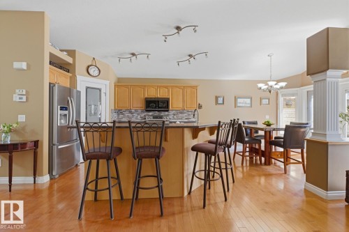 Open-concept kitchen and dining area featuring warm wood-finish flooring, light wood cabinetry, a stainless steel refrigerator, and a tiled kitchen backsplash - 9 Danfield Place, Spruce Grove, AB - Indoor Photo Showing Kitchen